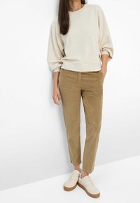 Sweat-shirt beige à épaules tombantes, associé à un pantalon en velours côtelé marron clair et des baskets blanches avec une semelle en gomme. Texture lisse dans l'ensemble.