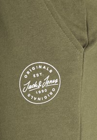 Sweatshirt vert olive avec un logo circulaire blanc portant "ORIGINALS EST. 1990 Jack & Jones." Texture lisse avec un tissu côtelé.