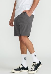 Gray shorts with a textured fabric, side pockets, paired with black sneakers and white socks featuring a black logo. Casual look.