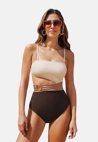 Hochgeschnittener Bikini in Beige und Braun. Das Oberteil verfügt �über ein trägerloses Design mit einem schrägen Schnitt. Ein dekorativer Gürtel mit einem Akzentdetail ist enthalten.
