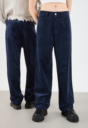 Donkerblauwe corduroy broeken met wijde pijpen, voorzien van een hoge taille, voortassen en een rafelige zoom aan de achterkant. Gecombineerd met zwarte plateau schoenen.