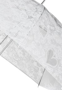 Ombrello bianco in pizzo con motivo floreale e ritagli a forma di cuore. Presenta una struttura in metallo argentato per supporto e durata.