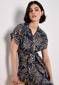 Vestido camisero azul marino con un patrón de hojas en beige, con botón en la parte delantera, mangas cortas y un cinturón en la cintura para dar forma. La tela parece texturizada.