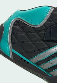 Chaussure de sport noire avec une texture matelassée, des accents turquoise, des bandes argentées, une semelle en caoutchouc et une zone d'orteil renforcée.