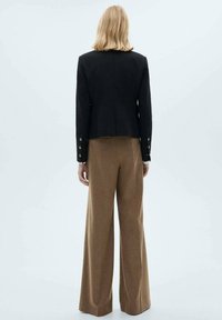 Black tailored jacket with a cropped design, gold button accents on cuffs, paired with wide-legged brown trousers in a soft texture.