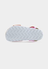 Σόλα σανδαλιού με λευκό κυματιστό σχέδιο πέλματος, ροζ και καφέ λουριά ορατά στις άκρες σε απλό φωτεινό φόντο.