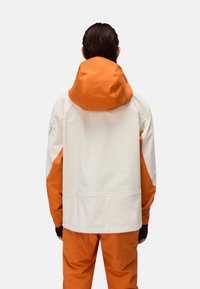 Chaqueta impermeable con un cuerpo blanco y detalles naranjas en la capucha. Diseñada con un corte relajado y puños ajustables para mayor comodidad.