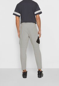 Šedé zúžené tepláky s černou náprsní kapsou; vyrobené z měkkého texturovaného materiálu; doplněné černobílým pruhovaným tričkem s krátkým rukávem.