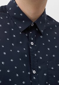 Camicia blu navy con bottoni, caratterizzata da un piccolo motivo bianco, colletto aperto e taschino sul petto; realizzata in un tessuto liscio con una texture morbida.