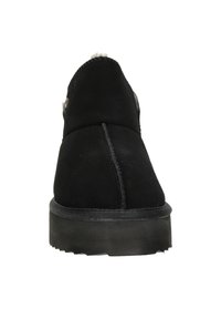 Zwarte suède enkelboot met een gestructureerde afwerking, verhoogde naad aan de achterkant en een rubberen zool met een lichte hak. Metaalaccent aan de zijkant.