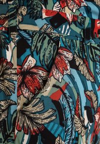 Floral-patterned fabric featuring vibrant red and green leaves against a blue background. Textured cotton material with fine detailing.
