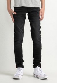 Černé skinny džíny vyrobené z denimu, s středním pasem, klasickým pěti-kapsovým designem a mírným vyblednutím, v kombinaci s bílými teniskami.