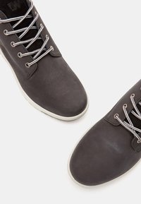 Zapatos de cuero grises con superficie texturizada y cordones plateados, con suela de goma blanca, punta redondeada y diseño de corte bajo.