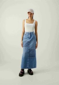 Saia maxi de ganga com um design em patchwork em tons de azul claro, apresentando uma cintura alta e bolsos laterais. Acessório com sapatos de plataforma.