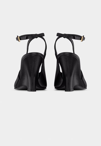 Ζευγάρι μαύρα γόβες με λουράκια στο πίσω μέρος και χρυσές αγκράφες, παρουσιασμένα από πίσω σε λευκό φόντο.