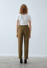 Olijfgroene high-waisted broek met een gladde textuur, gecombineerd met een witte aansluitende t-shirt. Zwarte hakken maken de outfit af.