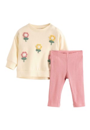 Kermanvärinen vauvan pitkähihainen paita, jossa keltaisia ja vaaleanpunaisia kukka-applikaatioita, yhdistettynä resorisiin vaaleanpunaisiin leggingseihin valkoisella taustalla.