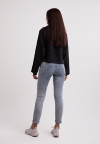 Czarny krótki sweter o teksturowanym wykończeniu, w połączeniu z jasnoniebieskimi dżinsami z podwiniętymi nogawkami oraz białymi trampkami.