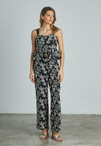 Jumpsuit nero a fiori con top peplum, caratterizzato da motivi floreali bianchi, gamba larga e spalline sottili. Tessuto liscio e dettagli strutturati.