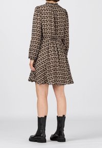 Hnědé šaty s květinovým vzorem a dlouhými rukávy, s elastickým pasem a délkou ke kolenům. Spárované s černými kotníkovými botami. Lehký materiál.