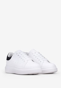 Sneakers bianche con una tomaia in materiale sintetico liscio, punta rotonda e chiusura con lacci a sei fori. Accentatura nera sul tallone, suola piatta in gomma.