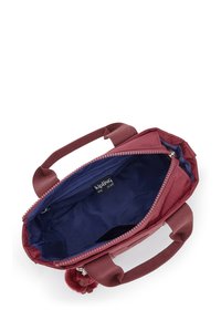 Röd nylonväska med dragkedjestängning, dubbla korta handtag och en mjuk innerslang. Innehåller en logotypklistermärke och en pom-pom-accessoar.