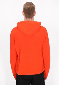 Czerwona bluza z kapturem, wykonana z miękkiego materiału, z kapturem regulowanym sznurkiem, długimi rękawami i elastycznym dołem. Prosta, w jednolitym kolorze, bez wzorów.