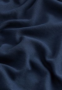 Mekana, tamnoplava tkanina s suptilnim naborima i nježnom teksturom, prikazujući detalje pletenog materijala i lagane varijacije sjenčanja.