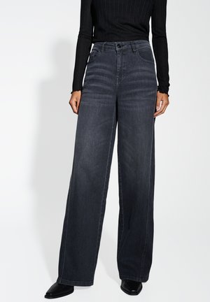 Wijd pijpen donkere grijze denim jeans met hoge taille, vijf zakken en contrasterende stiksels. Gecombineerd met een zwart ribbel langemouwen top.