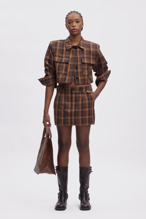 Brown and yellow plaid cropped jacket with two front pockets, paired with a matching skirt. Brown leather bag and knee-high black boots.