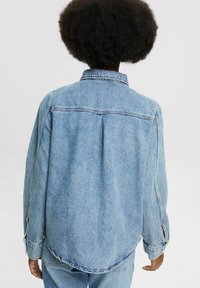 Jeansjacka i ljusblått. Har krage, långa ärmar och böjd nederkant. Baksidan har en central söm och lite plissé-detalj.