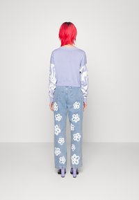 Light purple cropped sweater with white patterned sleeves, paired with light blue jeans featuring embroidered white flower designs. Purple block heels.