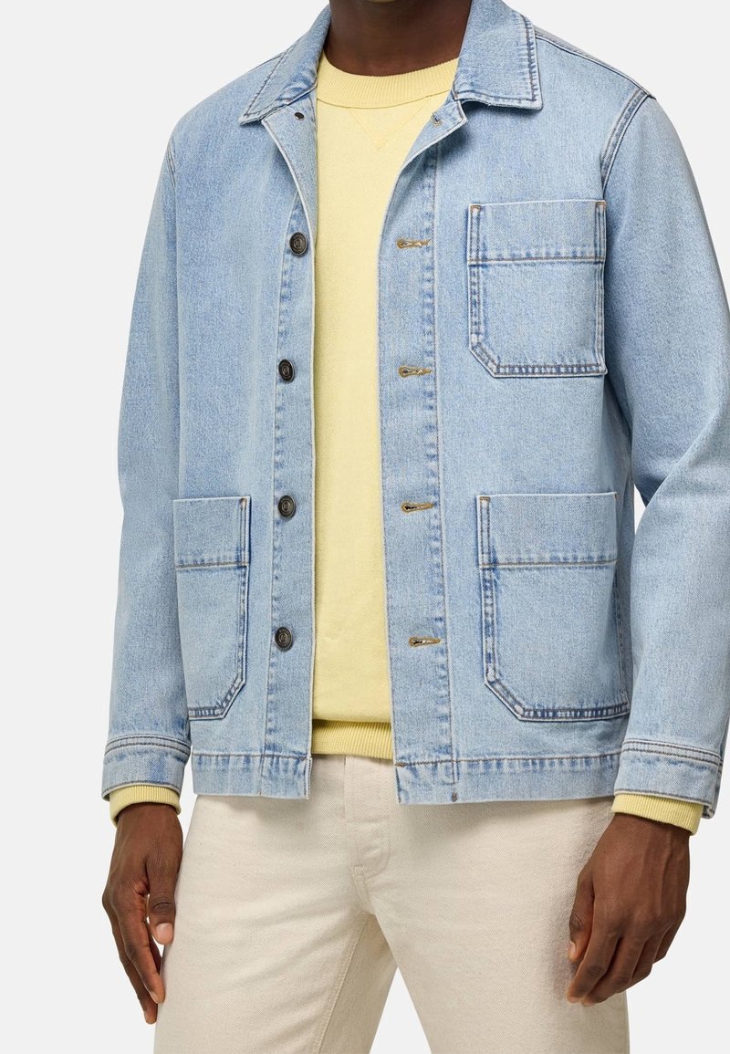 Vaaleansininen farkkutakki kauluksella, etutaskuilla ja napitettavalla edessä, päällystettynä pastellikeltaisella neuleella. Sileä koostumus, rento istuvuus.