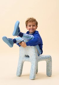 Sneakers blu con accenti a contrasto, maglietta blu e pantaloni a righe blu chiaro. Seduto su una sedia tessurizzata bianca e blu puntinata.