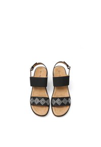 Sandal nero con una fascia larga, caratterizzata da un motivo geometrico in argento su una banda nera. Soletta morbida color tan e cinturino alla caviglia regolabile.