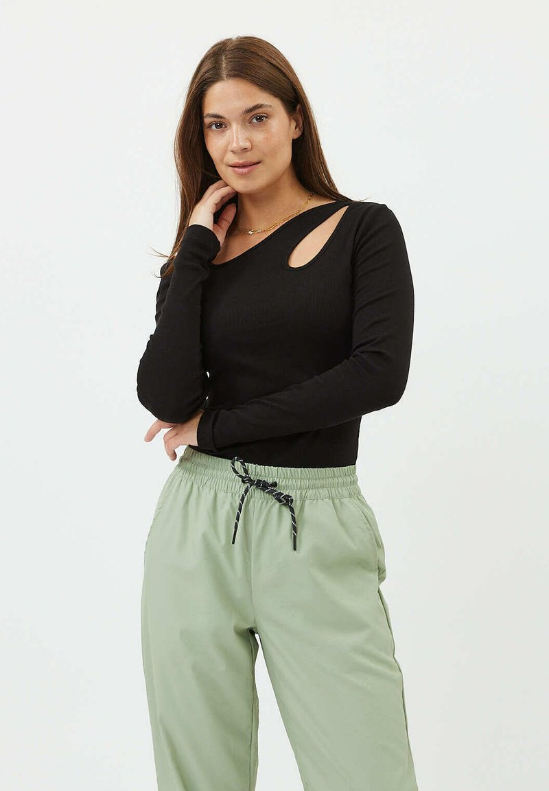 Zwart lang mouwtop met een ribbeltextuur, voorzien van een uitsnijding op de linker schouder, gecombineerd met lichtgroene broek met aantrekkoord.