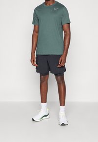 Zielona koszulka z krótkim rękawem z białym logo, czarne szorty, białe trampki z zielonymi akcentami i teksturowaną podeszwą, noszone z białymi skarpetkami.