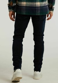 Jeans ajustados de color azul oscuro con una textura suave y detalles de costura mínimos, combinados con zapatillas blancas que tienen una suela texturada.
