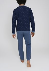 Completo di pigiama blu navy con una maglia a maniche lunghe a fantasia e pantaloni blu uni. Tessuto morbido con polsini e vita a coste.