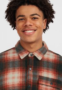 Rode en zwarte geruite flanellen shirt met knoopsluiting, kraag en borstzak met contrasterende witte vierkantjes. Zachte textuur.