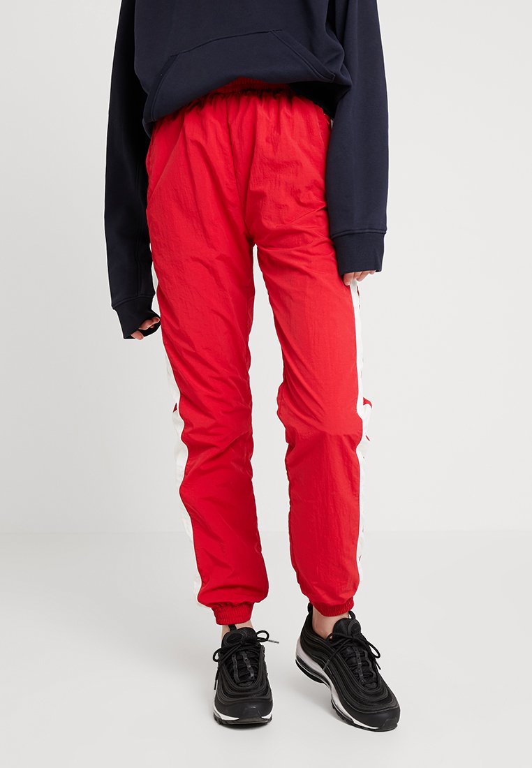 Červené ľahké športové nohavice s elastickým pásom a bielymi bočnými pruhmi, v kombinácii s tmavomodrým oversized sweatshirtom a čiernymi teniskami.