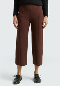 Bruine broek met wijde pijpen, gemaakt van textuurstof, met verticale naden en een hoge taille. Gecombineerd met zwarte veterschoenen.