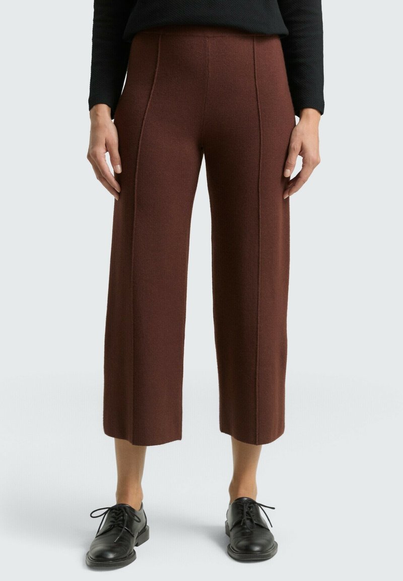 Bruine broek met wijde pijpen, gemaakt van textuurstof, met verticale naden en een hoge taille. Gecombineerd met zwarte veterschoenen.