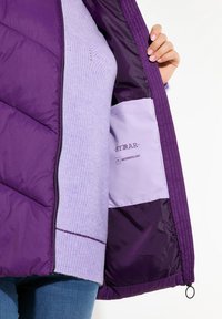 Lila Puff-Jacke mit gestepptem Muster, ausgestattet mit einer weichen Lavendel-Innenauskleidung und einer Tasche mit der Bezeichnung "wasserabweisend".