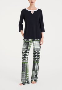 Top nero con scollatura bianca e dettaglio a chiave, abbinato a pantaloni larghi con fantasia in verde, nero e bianco a motivo geometrico.