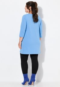 Hellblaues Tunika-Top mit Dreiviertelärmeln, kombiniert mit schwarzen Leggings und blauen High-Heel-Stiefeletten, mit einer glatten Textur.