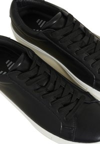 Baskets en cuir noir avec lacets noirs et semelles blanches, vues de dessus sur un fond blanc.