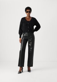 Cardigan nero fluffy con scollo a V, bottoni frontali e maniche a palloncino abbinato a pantaloni neri in pelle a gamba dritta a vita alta e tacchi.