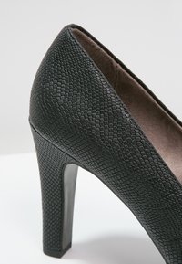 Zapato de tacón alto negro con un upper de piel sintética texturizada con un patrón de reptil y un tacón elegante y brillante.