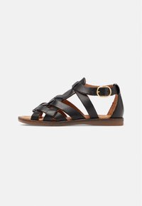 Černá kožená sandál s křížovými pásky, plochou podrážkou a nastavitelnou sponou u kotníku. Hnědá stélka se švy.